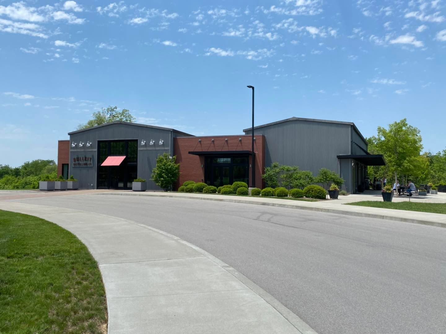Modern industrial building with gray and black exterior beside a curved road under a blue sky