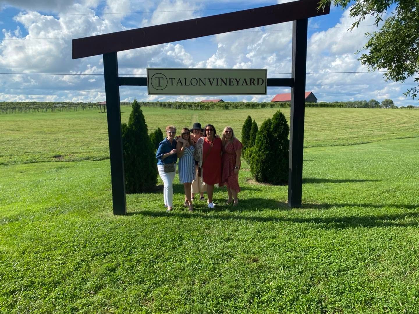 Group posing under a vineyard sign in a sunny green field