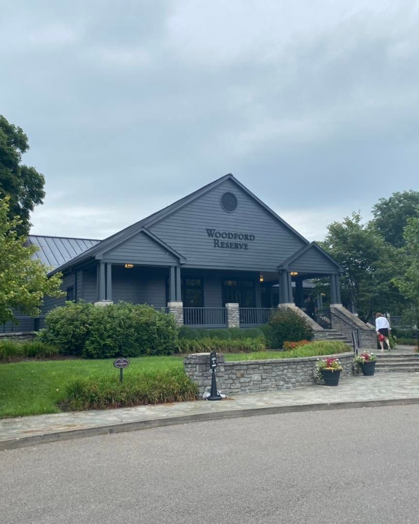 Gray building with a peaked roof, front steps, and landscaping under a cloudy sky.