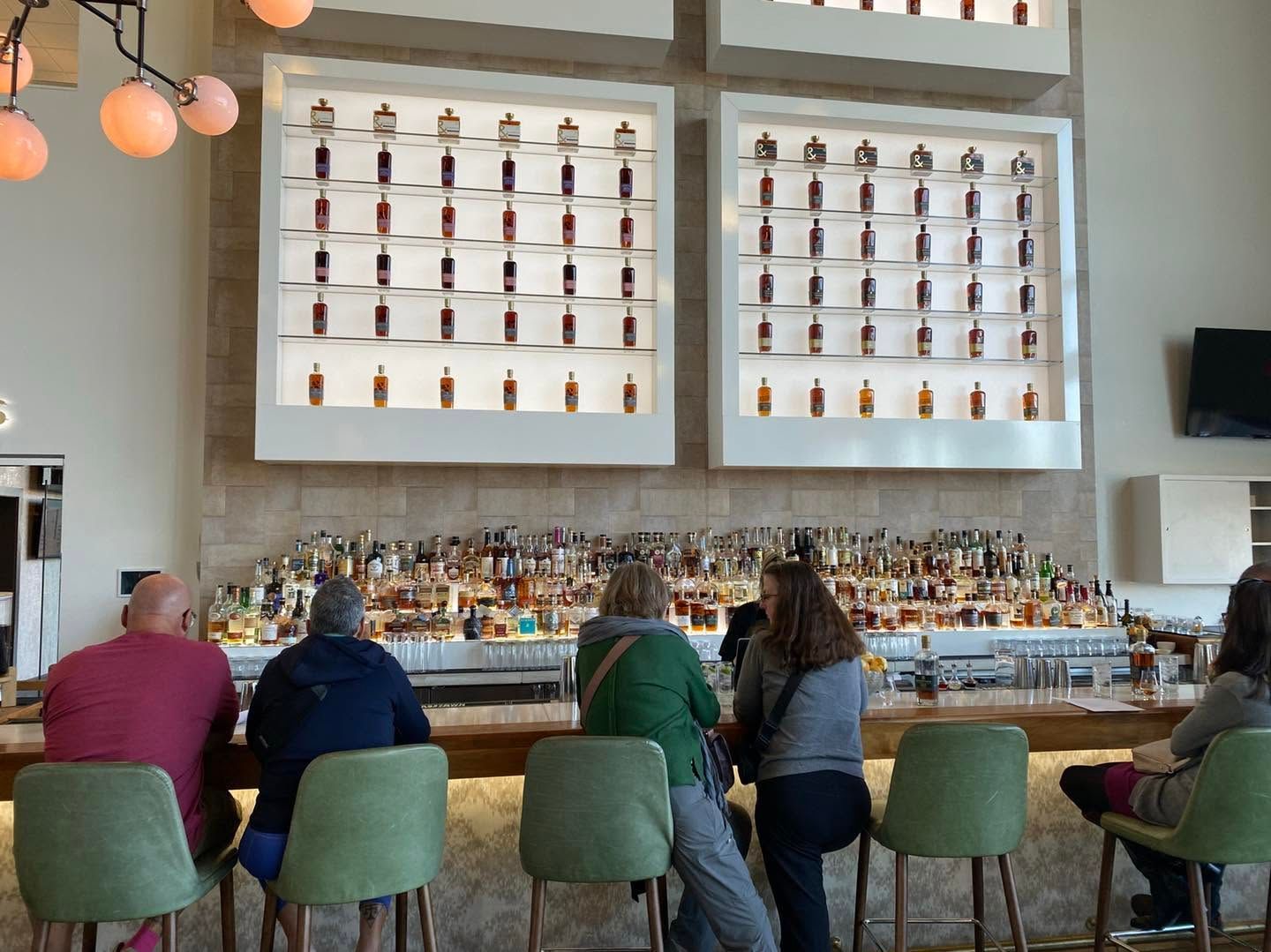 People seated at a bar with colorful stools beneath shelves of bottles and framed displays