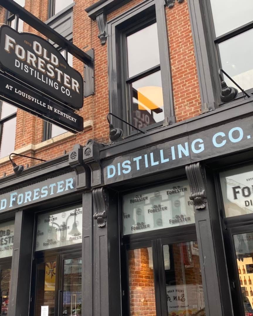 Storefront of Old Forester Distilling Co. with brick facade and black signage on a city street.