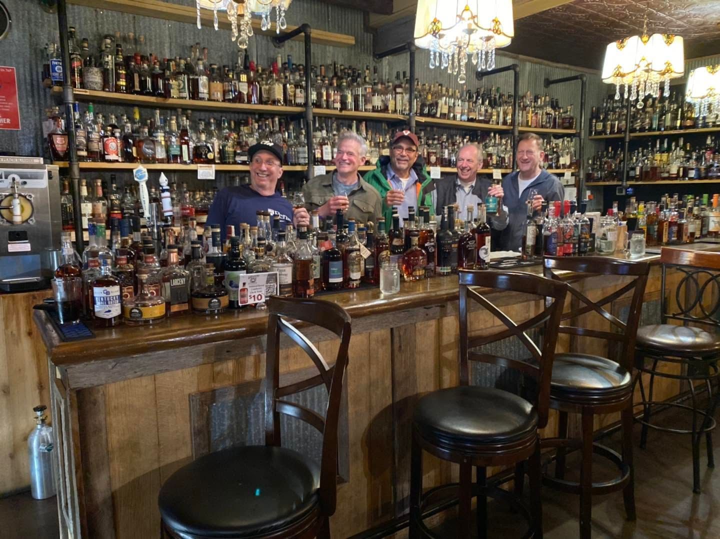 Bar with shelves of liquor bottles and three people standing behind the counter