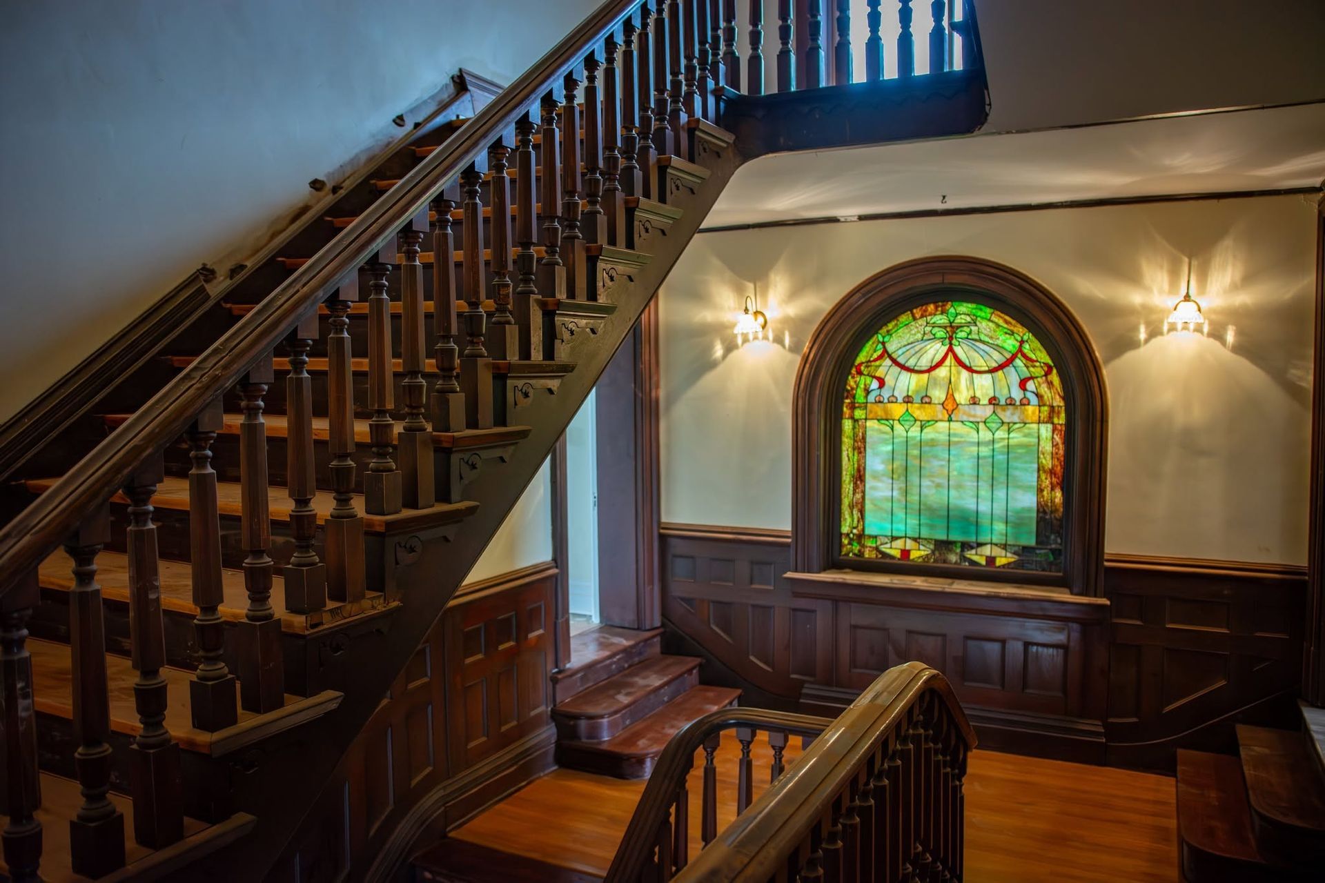 Wood-paneled staircase and landing with stained-glass window in a historic interior