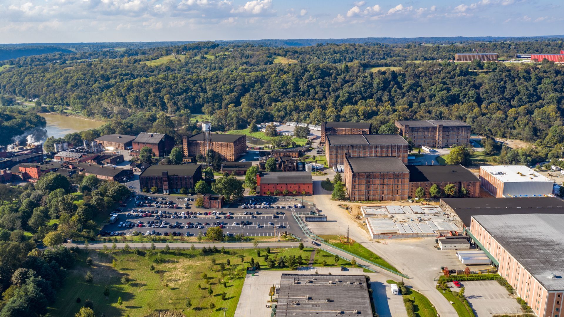 Aerial view of a campus with brick buildings, parking lots, and a forested hillside in the background