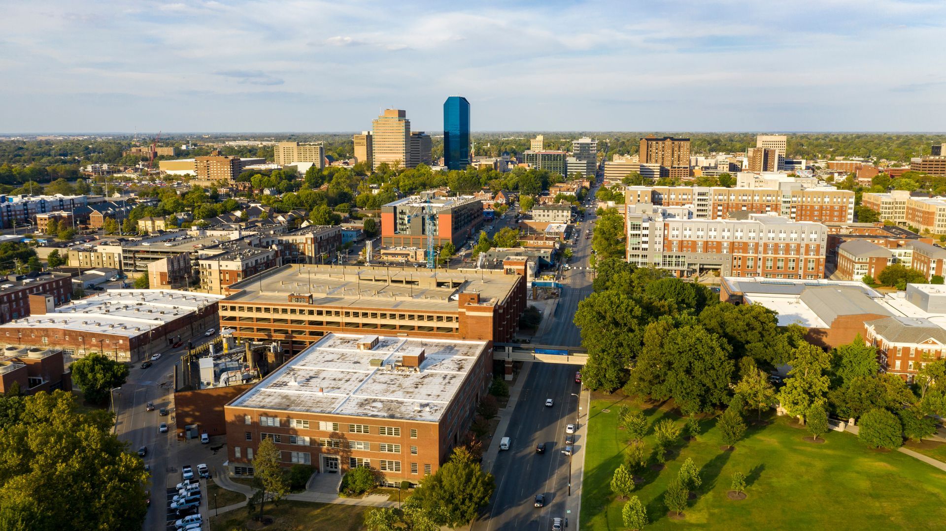 Aerial view of a city neighborhood with apartment buildings, tree-lined streets, and a distant downtown skyline