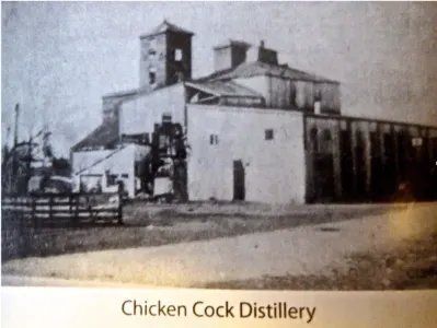 Black-and-white photo of the Chicken Cock Distillery building with a fence and tower.