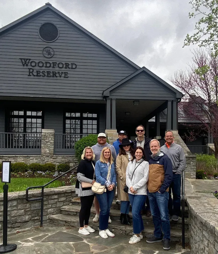 Group of people posing outside Woodford Reserve distillery entrance on a cloudy day.