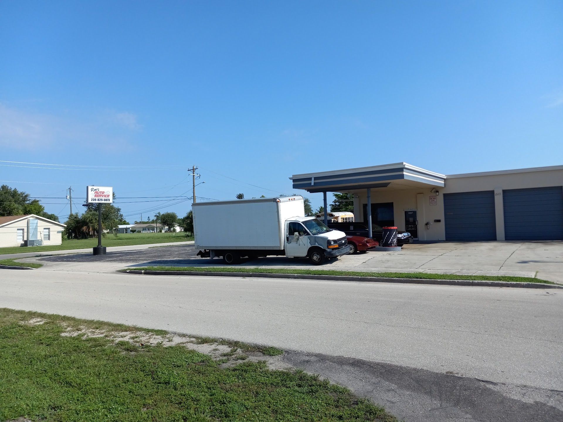 White box truck and red car parked beside a beige building with blue garage doors under a clear sky. | Ron's Auto Service