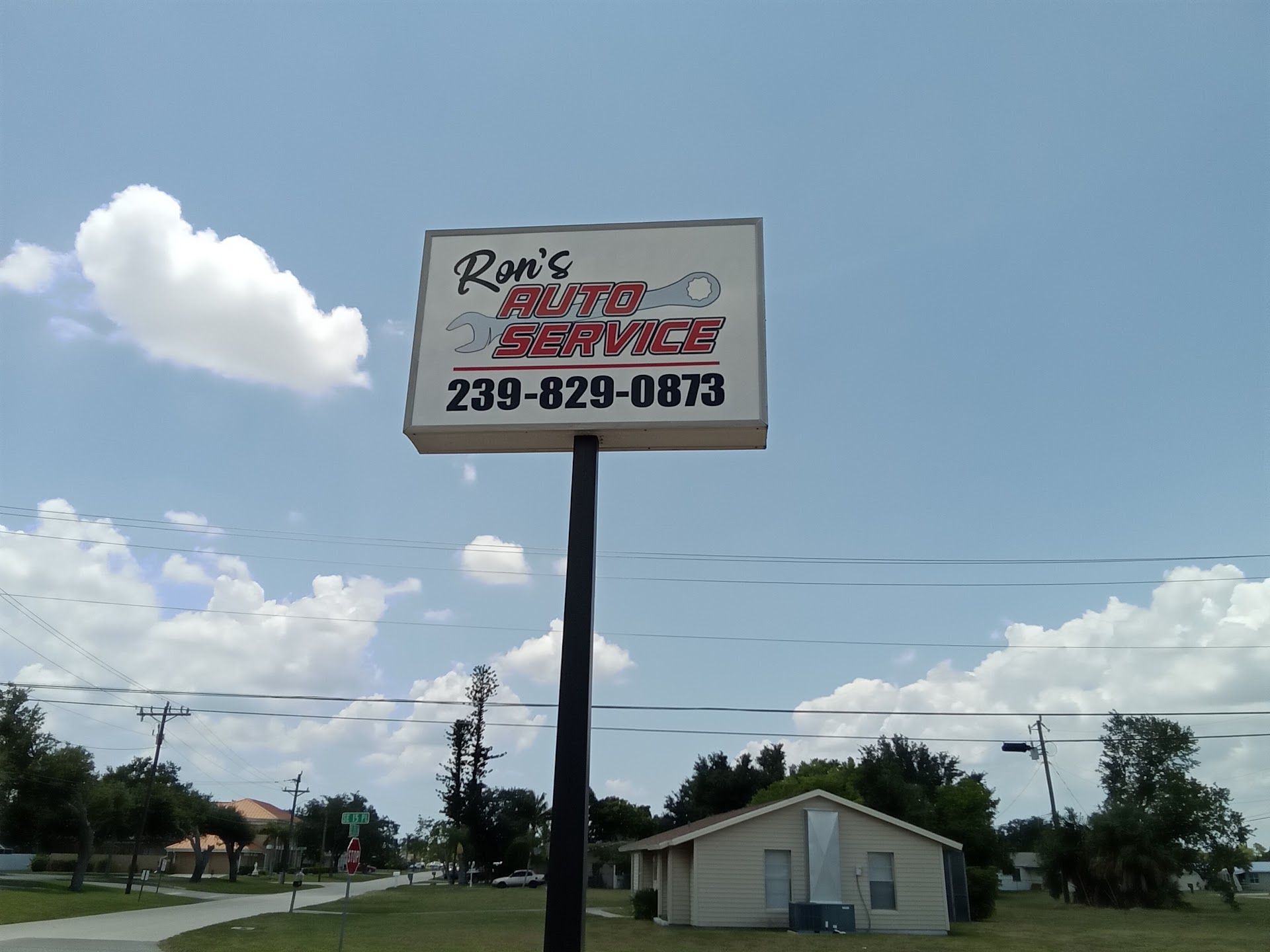 Roadside sign for Ron’s, with a phone number, against a blue sky and small building. | Ron's Auto Service