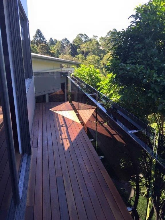 A Wooden Deck With a Glass Railing and Trees in the Background — Frameless Shower Installations In Maroochydore, QLD