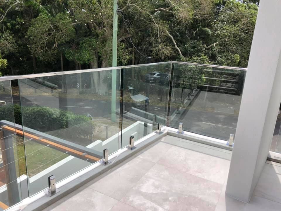 A Balcony With a Glass Railing and Trees in the Background — Frameless Shower Installations In Caloundra, QLD