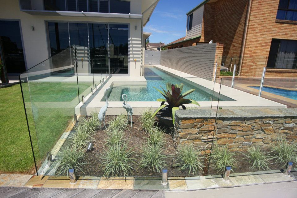 A Large Swimming Pool is Surrounded by a Glass Fence — Frameless Shower Installations In Maroochydore, QLD