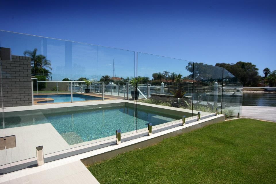 A Large Swimming Pool Is Surrounded By A Glass Fence — Frameless Shower Installations In Maroochydore, QLD