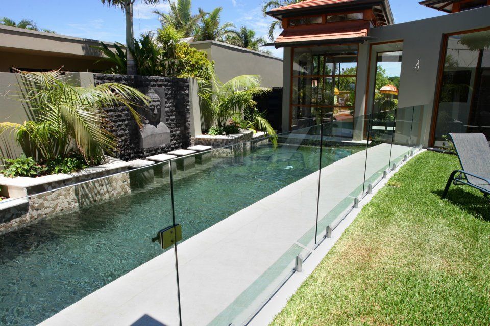A Large Swimming Pool is Surrounded by a Glass Fence — Frameless Shower Installations In Maroochydore, QLD
