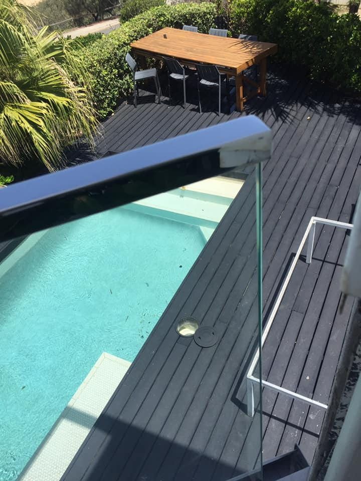 A Pool With a Dark Gray Deck and a Wooden Table With Chairs — Frameless Shower Installations In Maroochydore, QLD