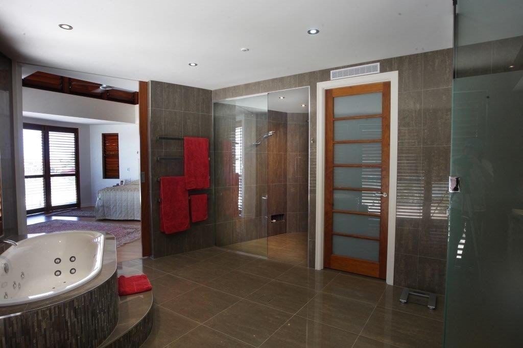 A Bathroom With a Jacuzzi Tub and a Glass Door — Frameless Shower Installations In Maroochydore, QLD