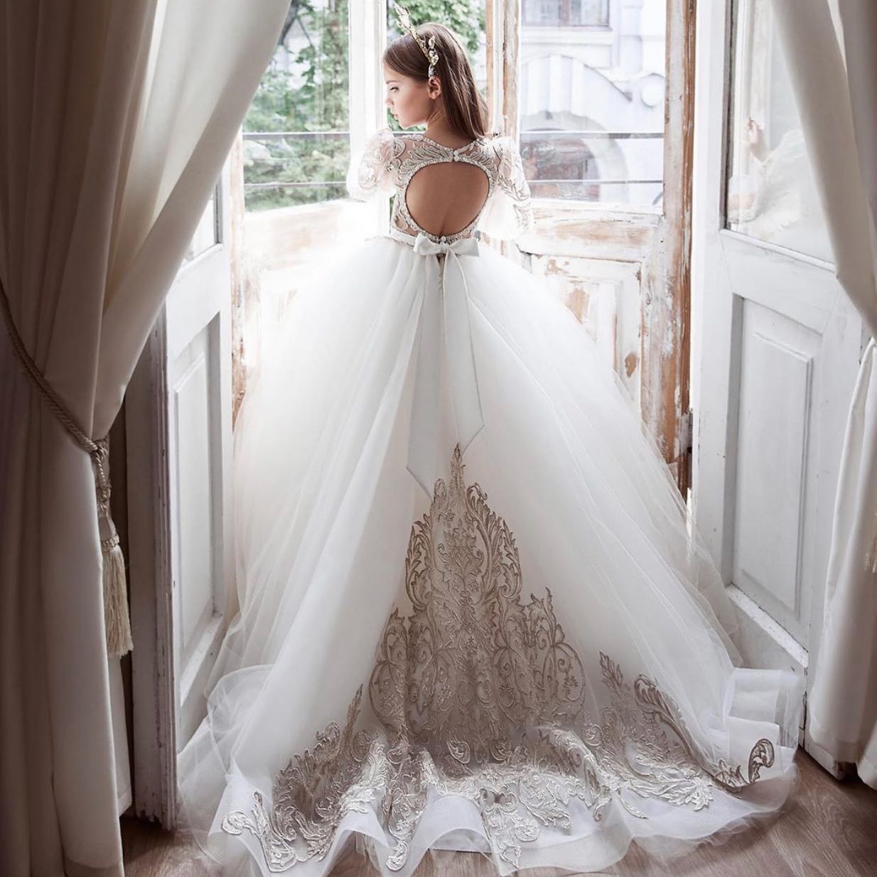 A woman in a white dress is standing in front of a window.