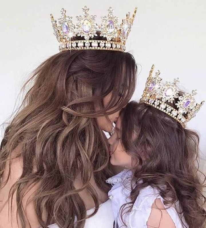 A mother and daughter wearing crowns are kissing each other.