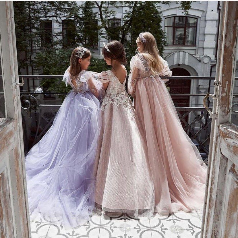 Three girls in long dresses are standing on a balcony