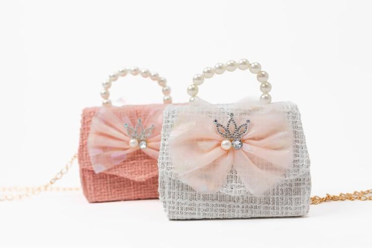 Two small handbags with bows and pearls on a chain on a white background.