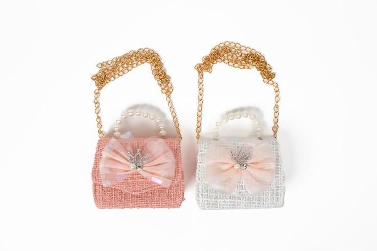 Two small handbags with bows and pearls on a chain on a white background.