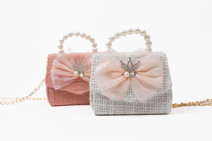 Two small handbags with pearl handles and bows on a white background.