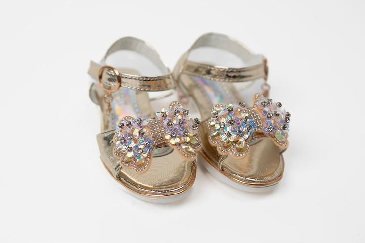 A pair of gold sandals with a bow on a white background.
