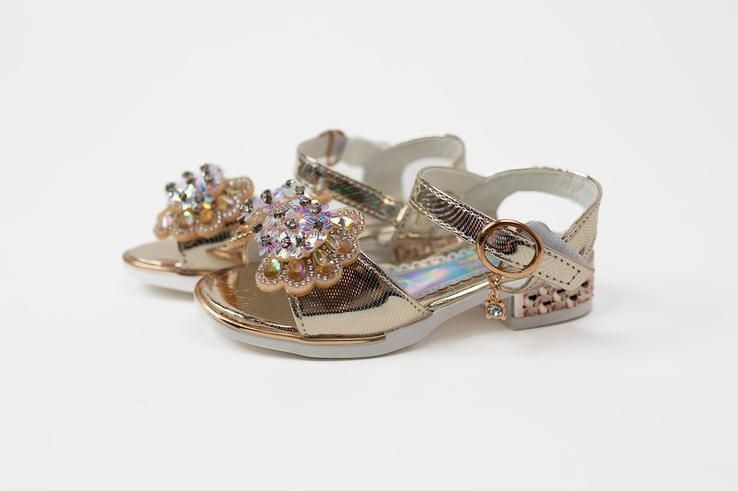 A pair of gold sandals with a bow on a white background.