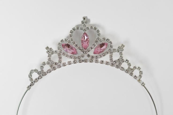 A white headband with a pink tiara on it on a white background.