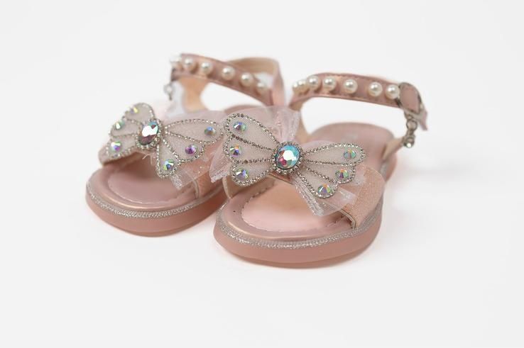A pair of pink sandals with a bow and pearls on a white background.