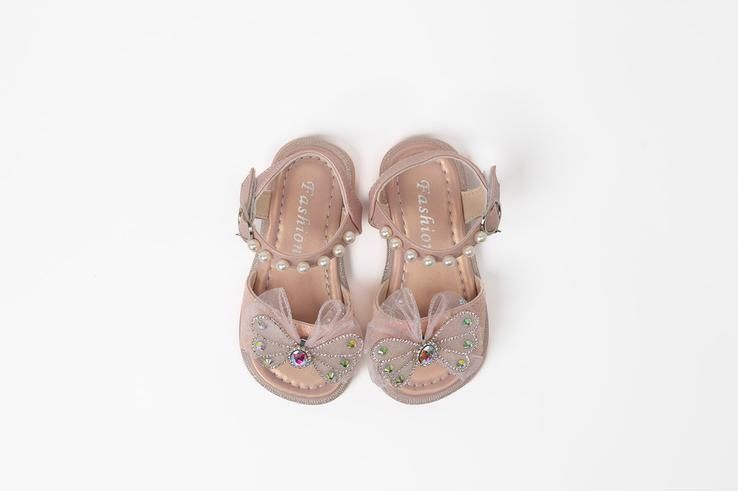 A pair of pink sandals with a bow and pearls on a white background.