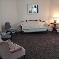 Quiet waiting room with a white sofa, chairs, a side table lamp, and a wall mirror
