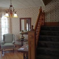 Cozy living room with armchair, staircase, chandelier, and floral wallpaper
