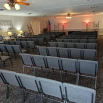 Empty meeting room with rows of gray chairs, ceiling fans, and an American flag at the front.