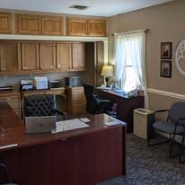 Home office with wooden cabinets, desk, computer, lamp, window, and chairs