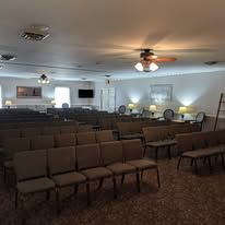 Empty church sanctuary with rows of brown chairs, ceiling fans, and a small stage area with music stands