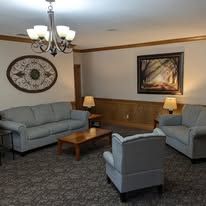Cozy living room with two gray sofas, armchair, coffee table, lamps, wall art, and chandelier