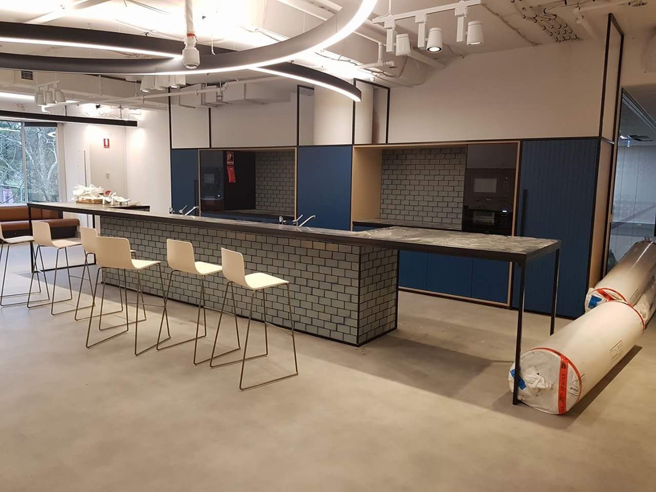 A Kitchen with A Long Counter and Chairs and A Roll of Carpet on The Floor — Sheridan Stone Aust in Yamba, NSW
