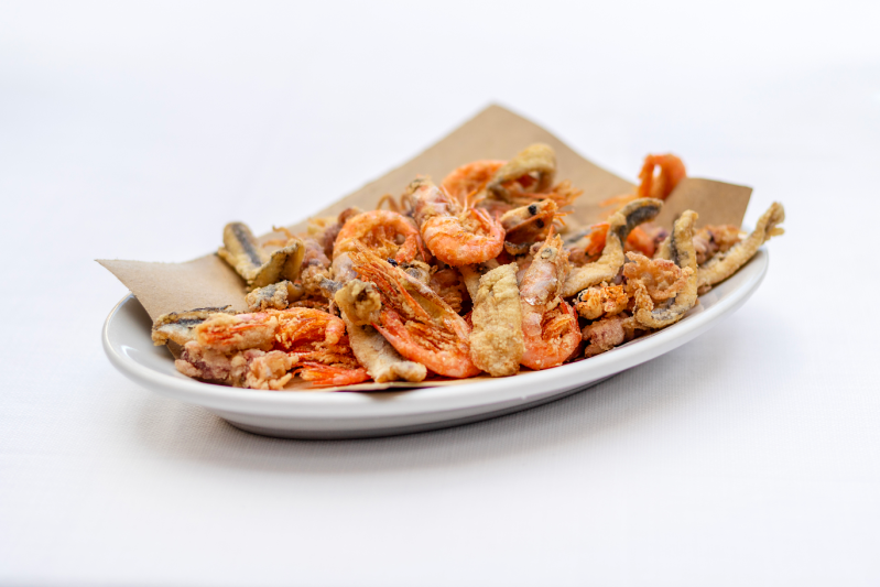 Piatto di pesce fritto: gamberi, pesce e calamari su un piatto bianco rivestito di carta marrone.