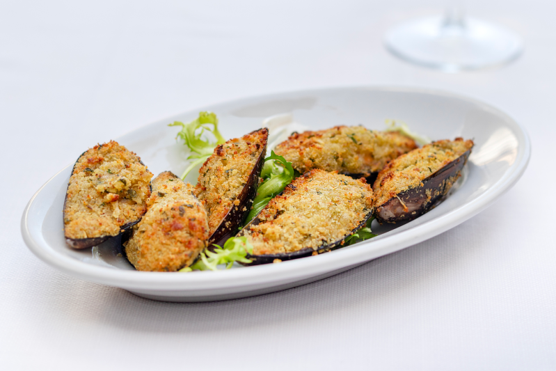 Cozze al forno con guscio su un piatto ovale bianco, guarnite con lattuga.