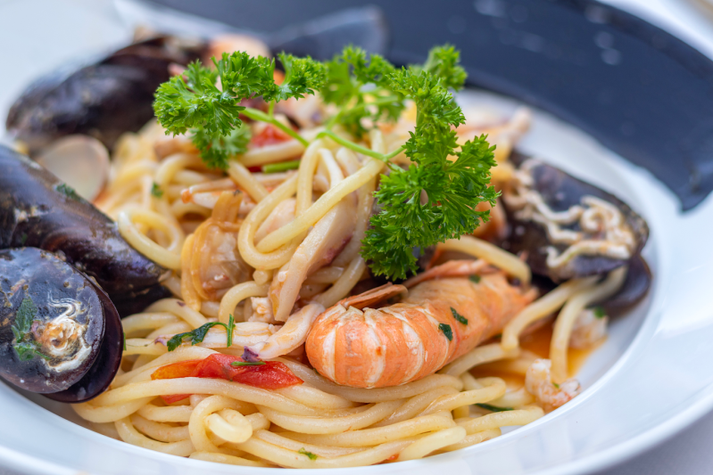 Piatto di pasta con cozze, gamberi e guarnizione di prezzemolo.