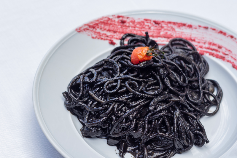 Spaghetti neri su un piatto bianco, conditi con un piccolo pomodoro rosso e salsa.