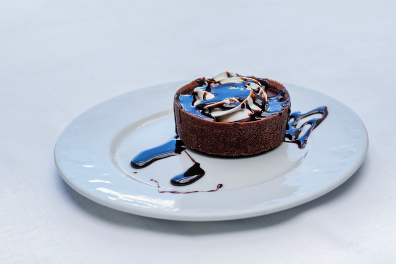 Crostata al cioccolato con salsa a filo e mandorle a lamelle su un piatto bianco.