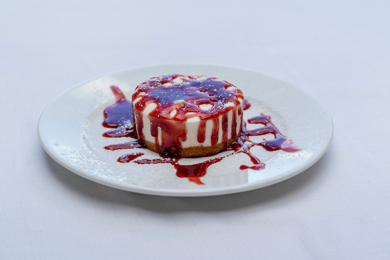 Cheesecake con salsa ai frutti di bosco su piatto bianco.