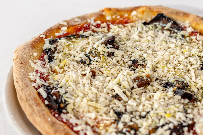 Pizza con funghi e formaggio bianco grattugiato su un piatto bianco.