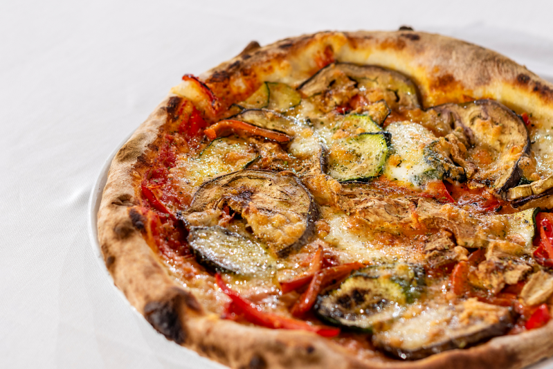 Pizza con melanzane, zucchine, peperoni rossi e formaggio su un piatto bianco.