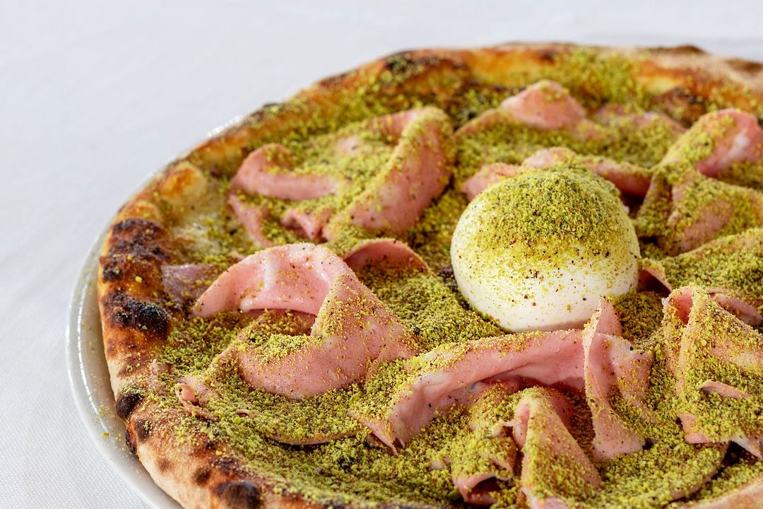 Pizza con mortadella, pistacchio e una cremosa palla di formaggio su un piatto bianco.
