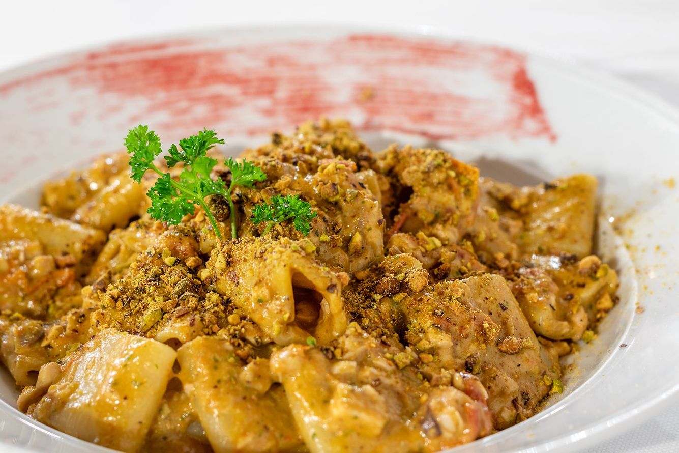 Piatto di pasta con salsa cremosa, guarnito con noci tritate e prezzemolo in una ciotola bianca.