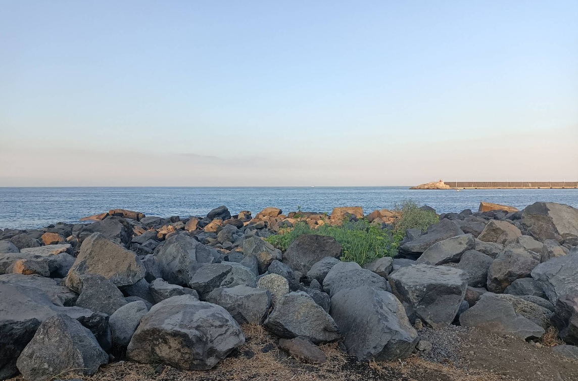 Costa rocciosa che si affaccia su un oceano calmo e un cielo limpido.