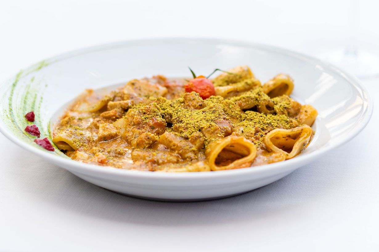 Piatto di pasta con salsa, pomodorini e pistacchi in una ciotola bianca.